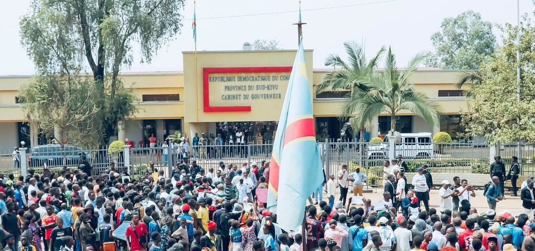 Des manifestants rassemblés devant le cabinet du gouverneur du Sud-Kivu, un drapeau de la RDC au premier plan